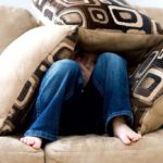 Kleiner Junge sitzt auf dem Sofa bedeckt mit Kissen