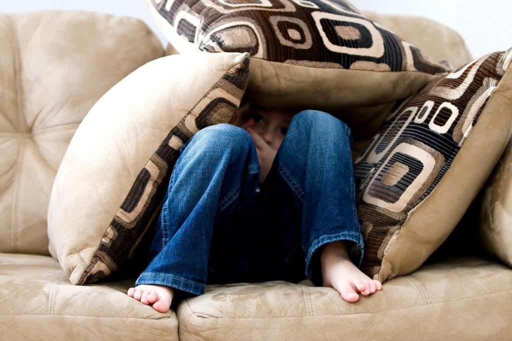 Kleiner Junge sitzt auf dem Sofa bedeckt mit Kissen