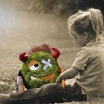 Mädchen sitzt traurig mit ihrem Kuscheltier im Gras