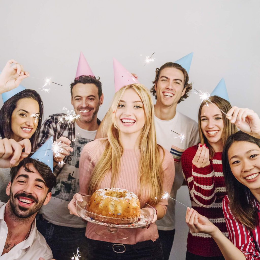 Eine Gruppe Menschen feiert mit Kuchen, Partyhütchen und Wunderkerzen.