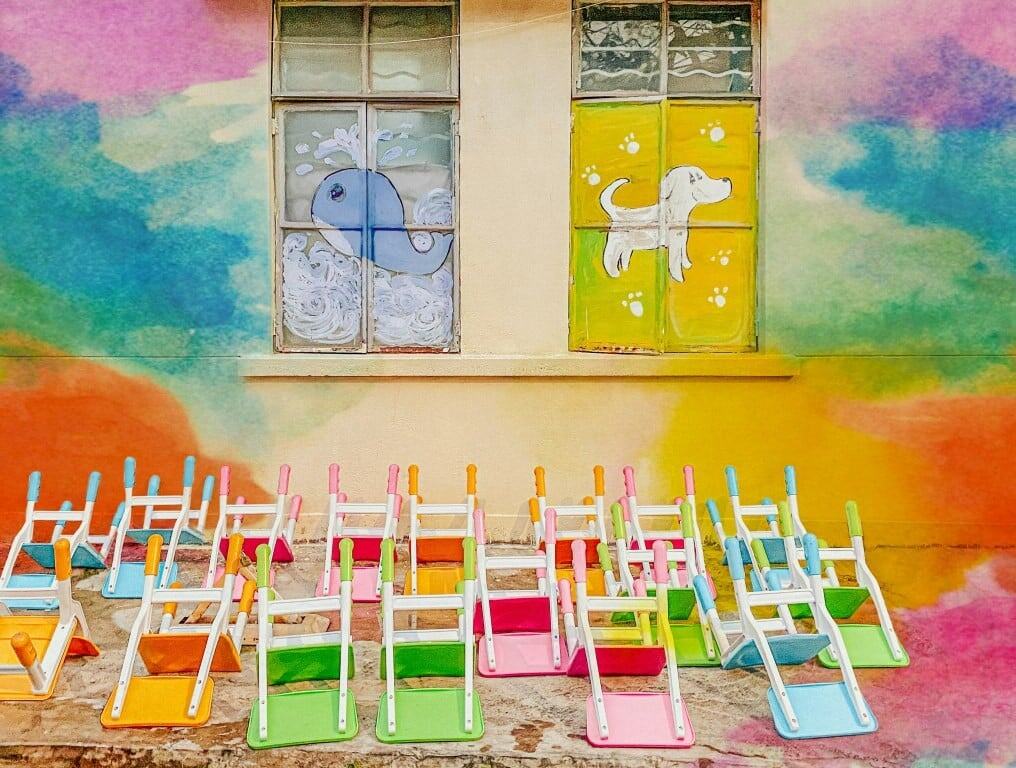 Umgedrehte bunte Kinderstühle vor einer bunten bemalten Wand | Foto von yue su auf Unsplash.com