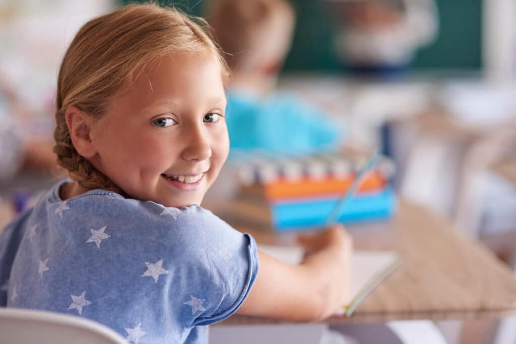 Schulstart mit Herz - Mädchen schaut fröhlich in der Schule